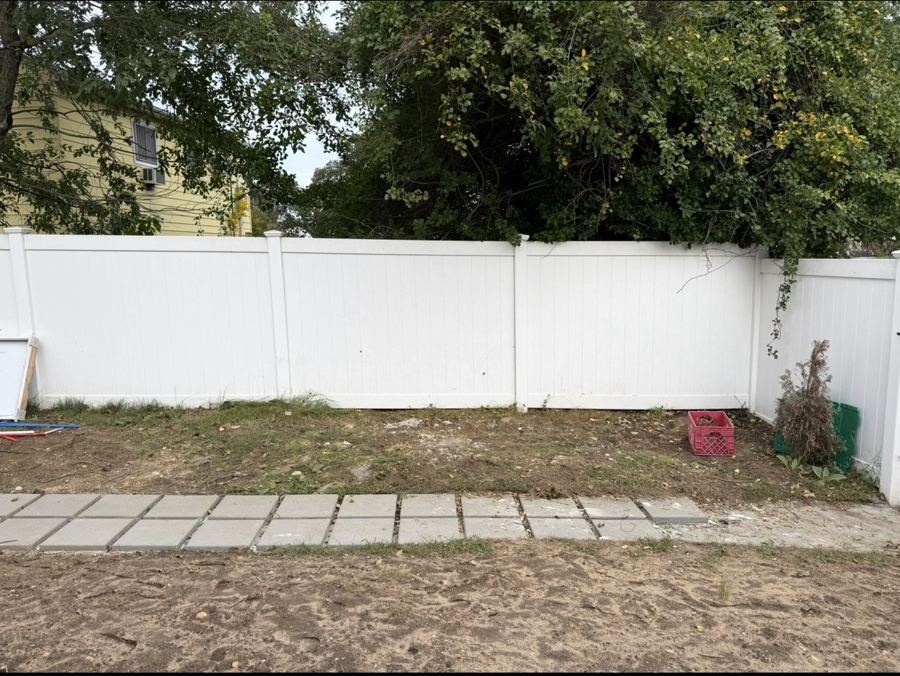 Backyard cleared along a white vinyl fence